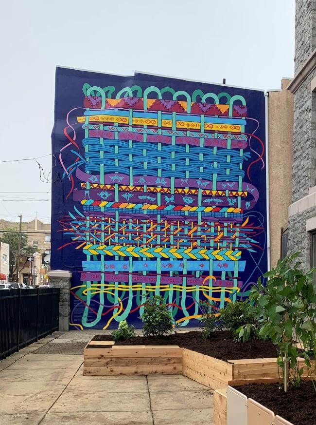 A two-story tall mural in an array of colors represents the theme of weaving.