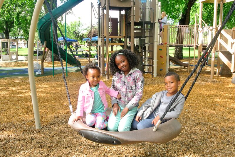 Three children sitting on a swing at a playground.