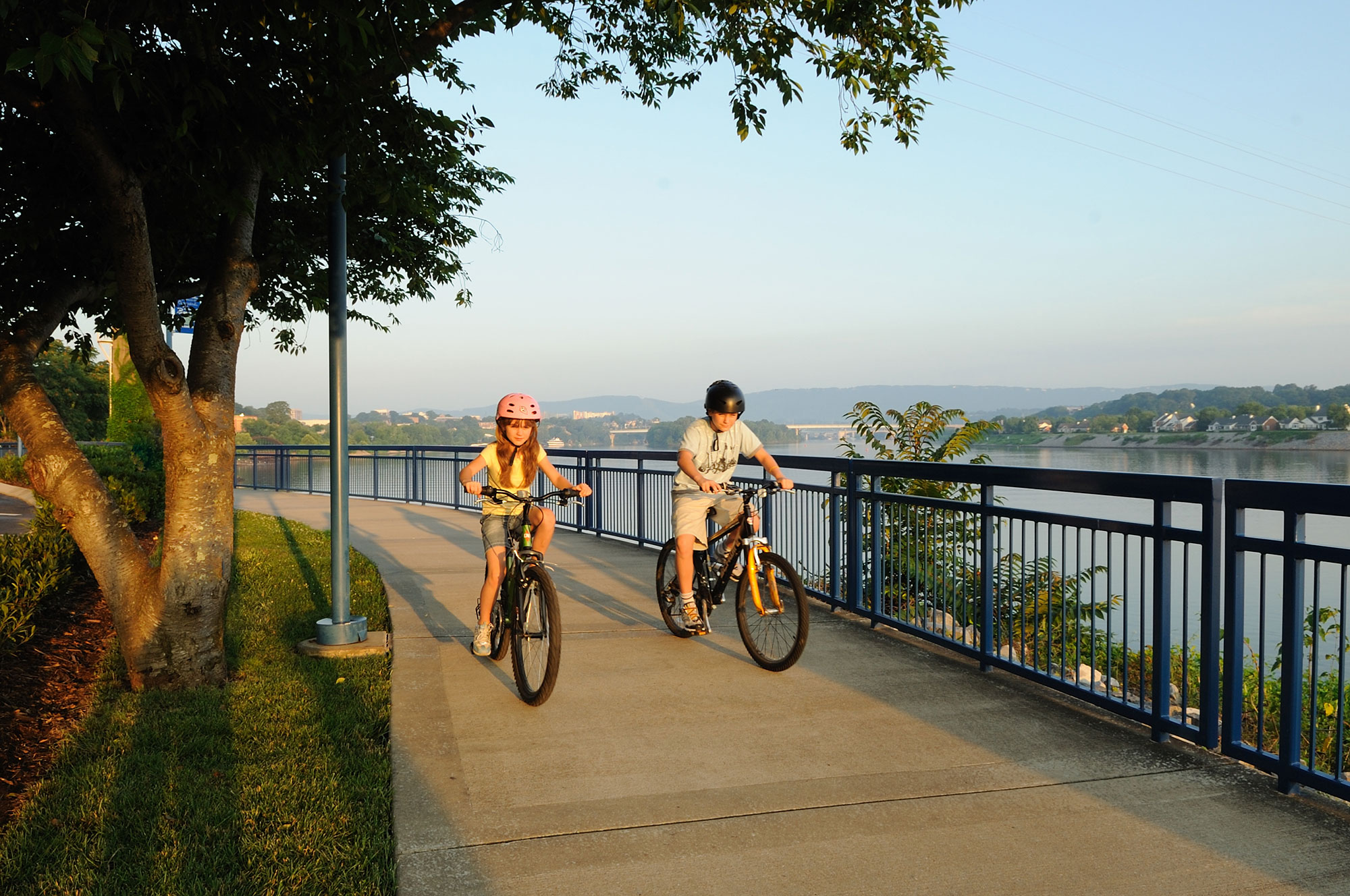 Two people riding bikes on a sidewalk next to a body of water.