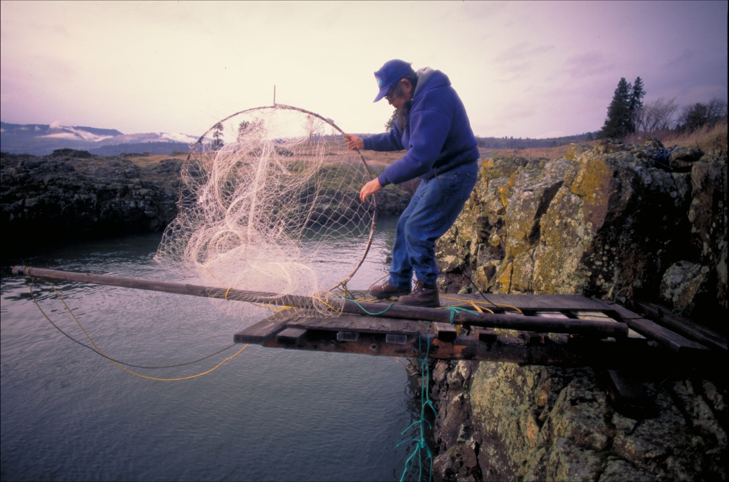 A man standing on a rocky ledge with a fishing net.