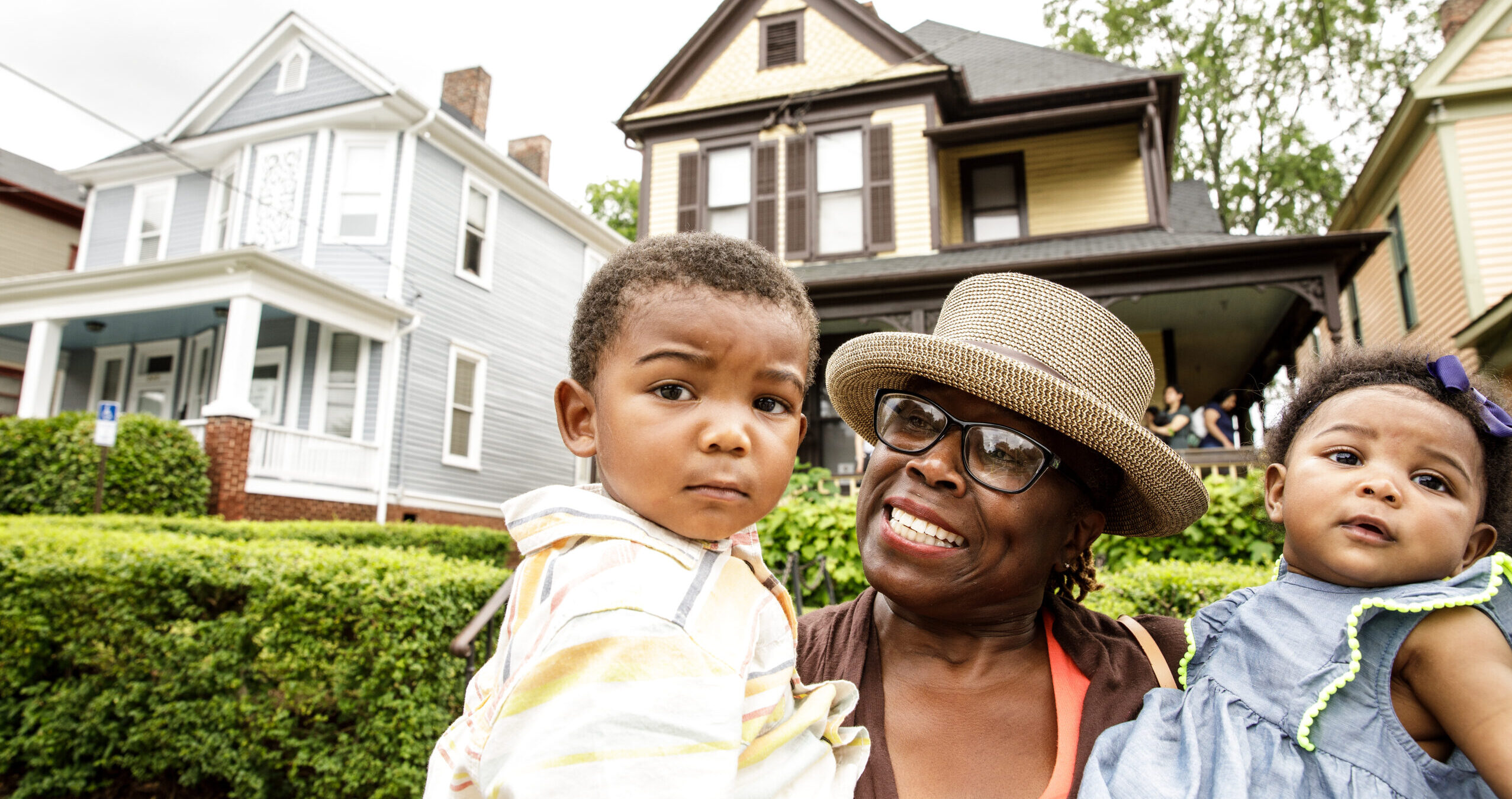 An african-american woman holding two children in front of a house.