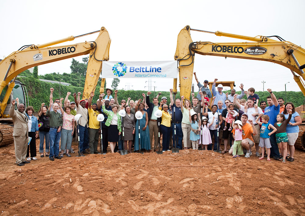 A group of people standing in front of an excavator.