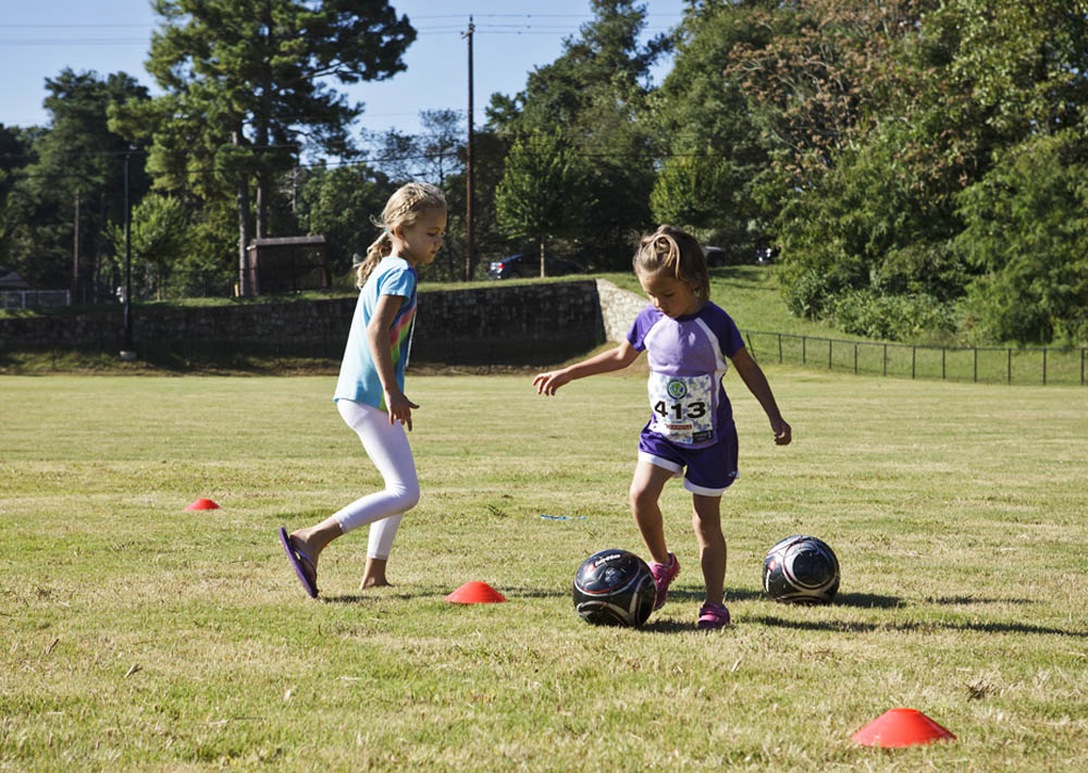 Two girls playing soccer on a grassy field.