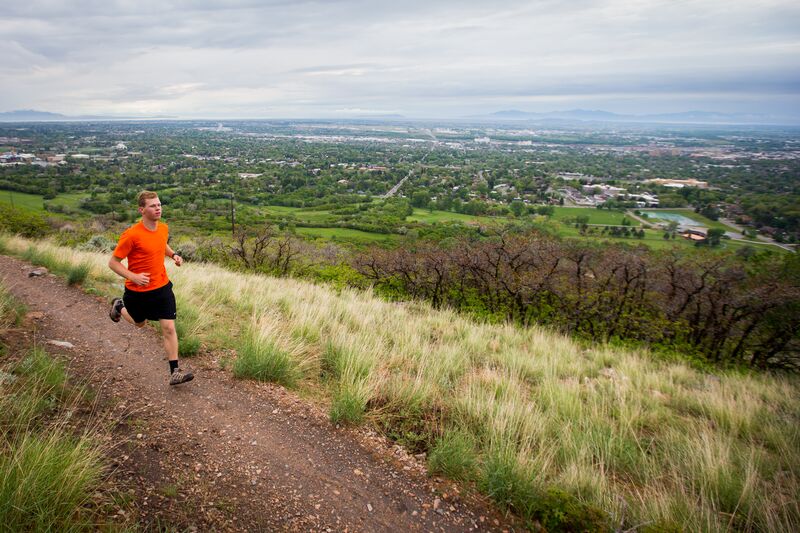 A man running on a trail with a view of a city.