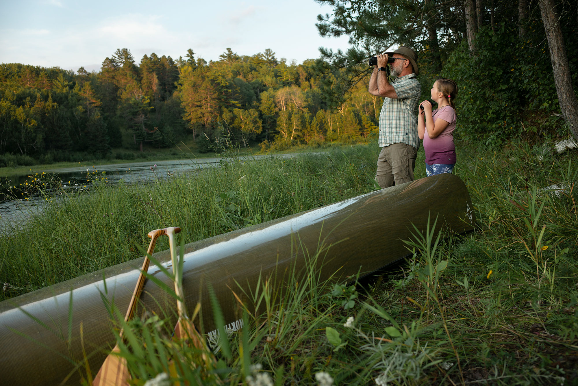 Two people looking at a canoe in the grass.