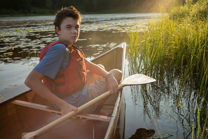 A young man in a canoe on a lake.