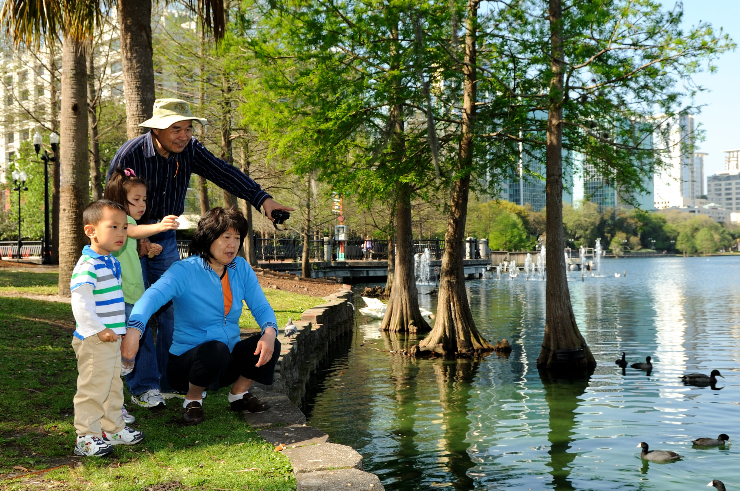 A family is standing near a pond with ducks.