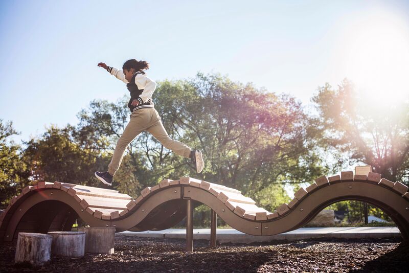 A boy jumping on a wooden structure in a playground.