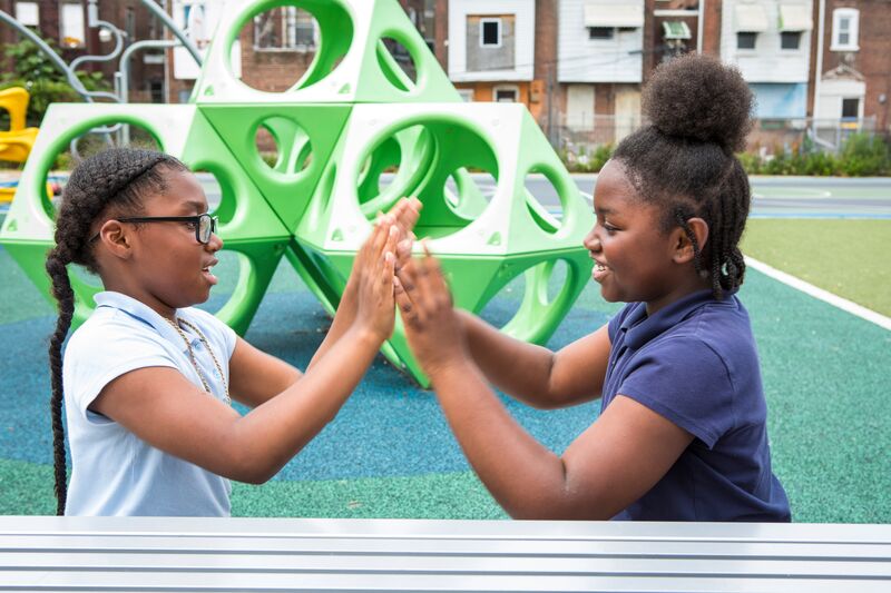 Two girls giving each other high fives in a playground.