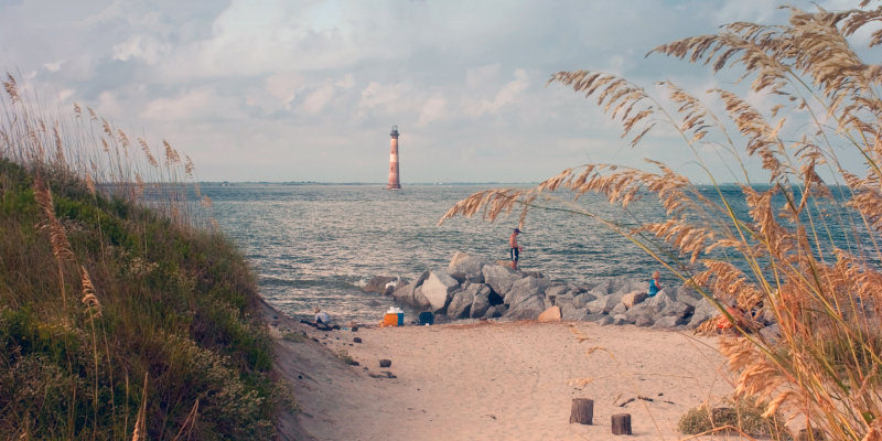 Lighthouse offshore of a sandy beach with people in the water