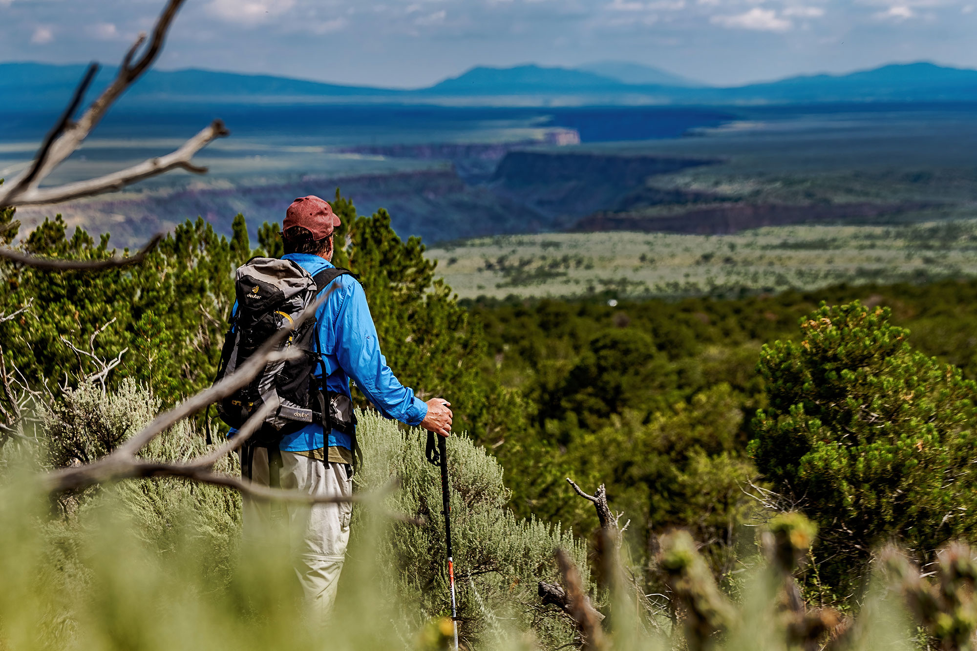 A man with a backpack and hiking sticks is looking out over a valley.