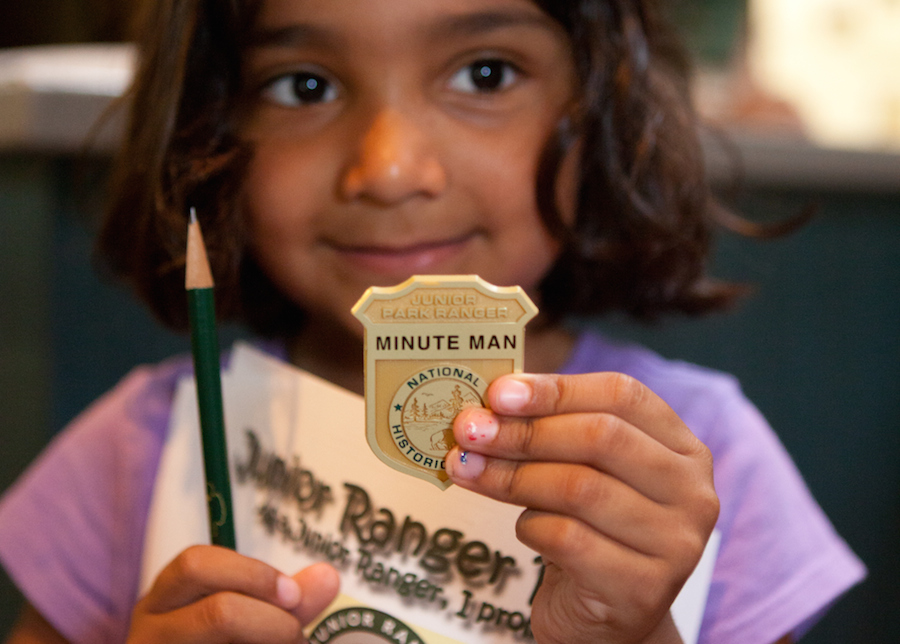 A young girl holds up her Junior Ranger badge.