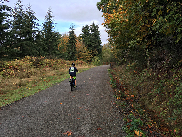 A boy rides his bike along a tree-lined trail