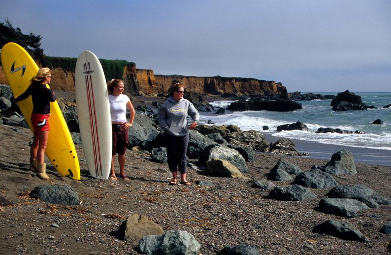 Three surfers wait for waves on a beach