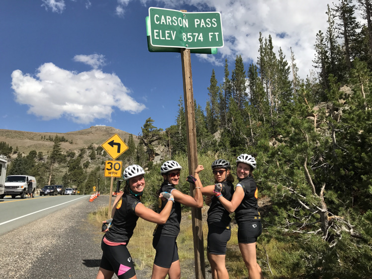Four cyclists pose under a sign reading "Carson Pass"