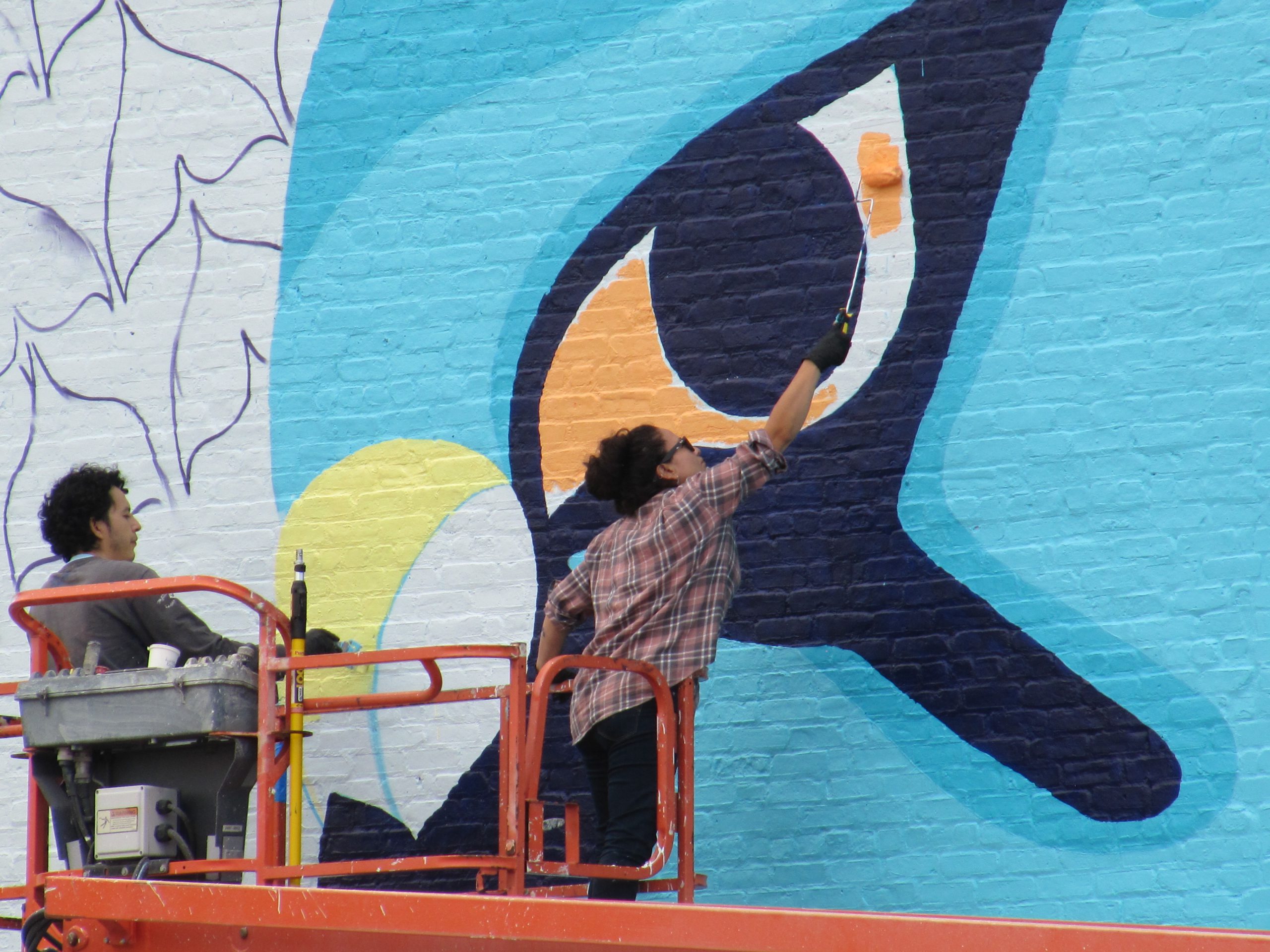 A woman on a lift paints a giant falcon eye with a roller
