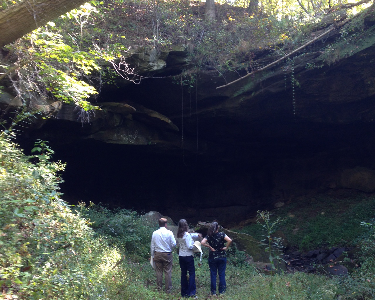 Three people stand at the mouth of a wooded cave
