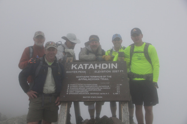 Six men stand behind a sign announcing the summit of Mt. Katahdin