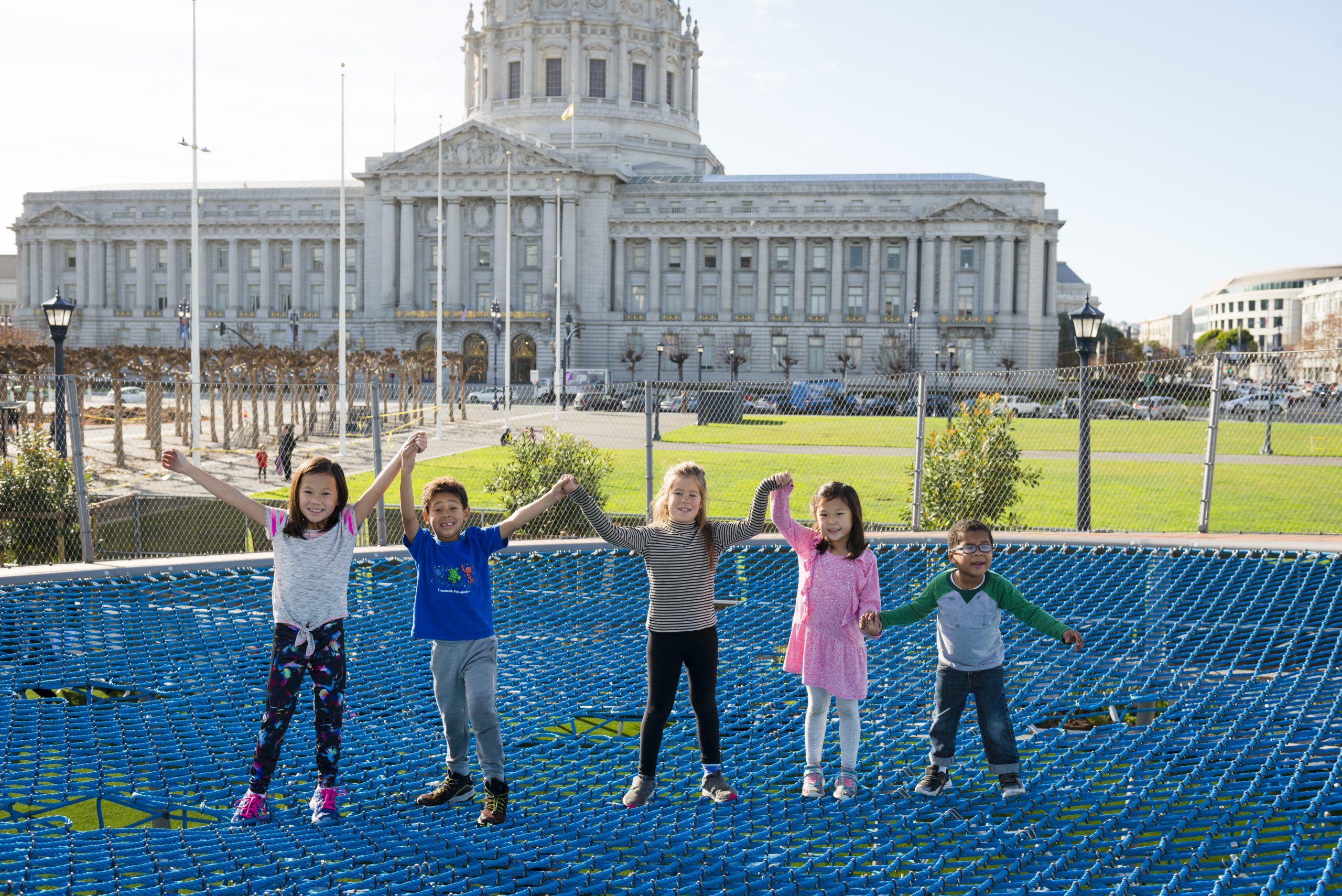 Kids stand on top of a play structure with SF City Hall in the background