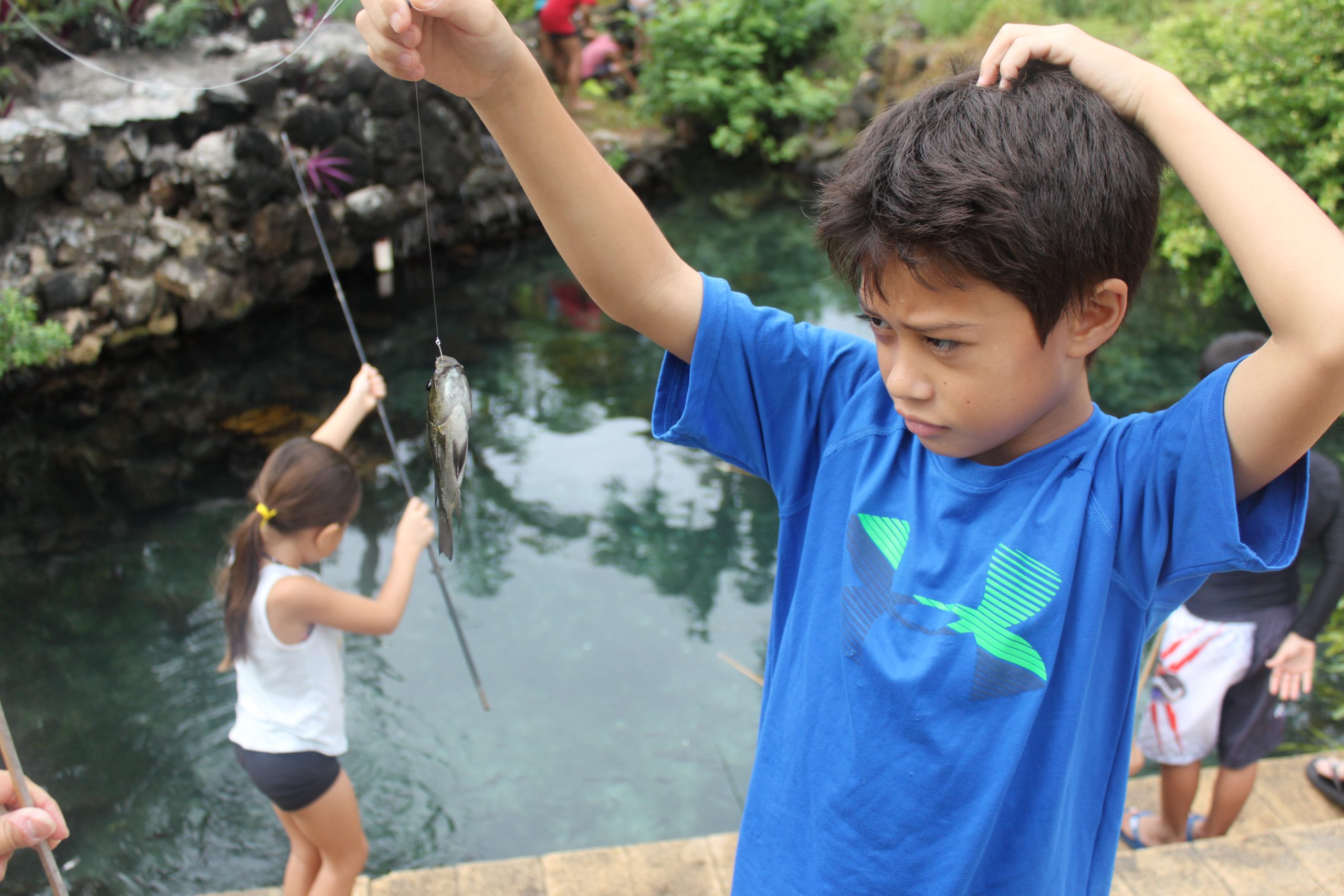 A boy looks at a fish on a pole