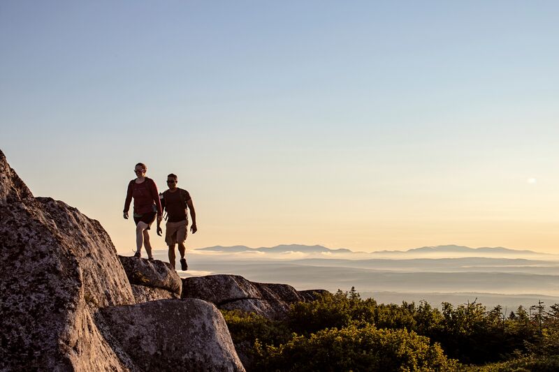 Two people walking on top of a mountain at sunset.
