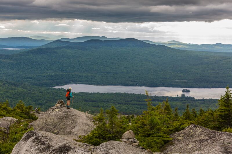 A person standing on top of a rock overlooking a lake.