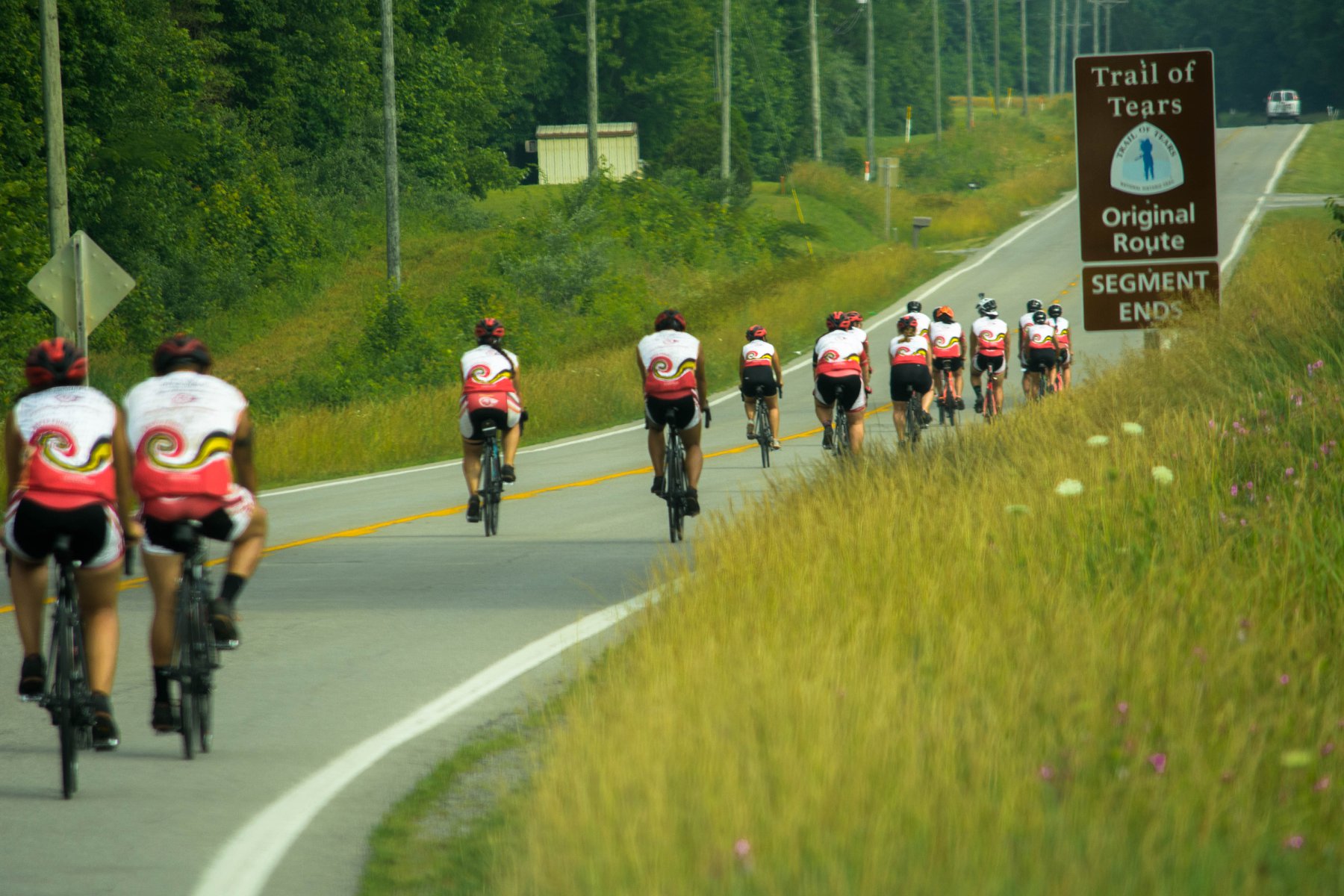 Cyclists ride past a sign reading "Trail of Tears Original Route"