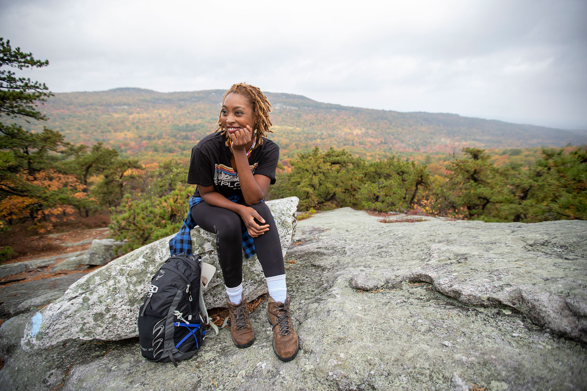 A woman sitting on top of a rock with a backpack.