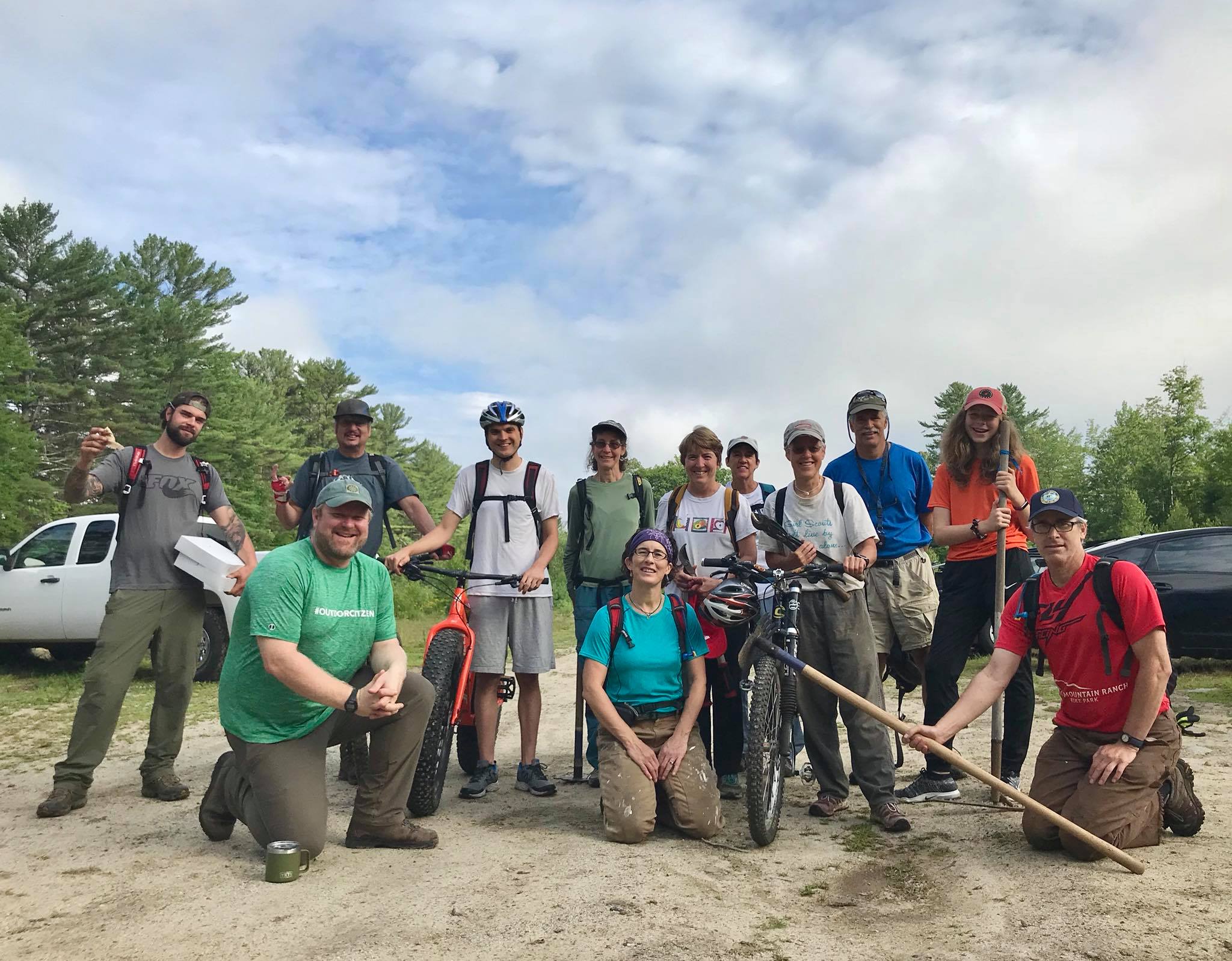 A trail crew poses for a photo with tools and bikes