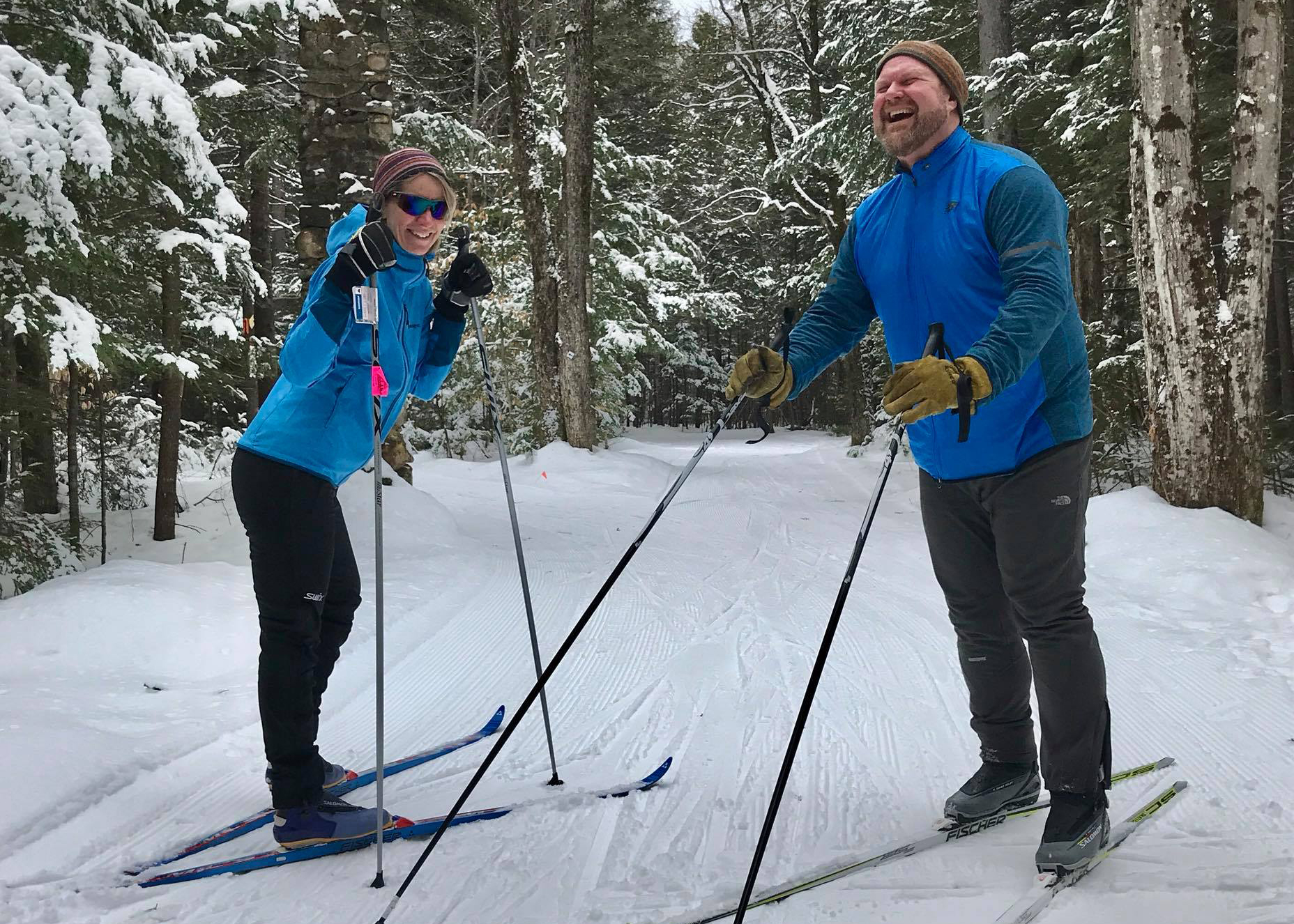 A man and a woman on cross country skis in a forest