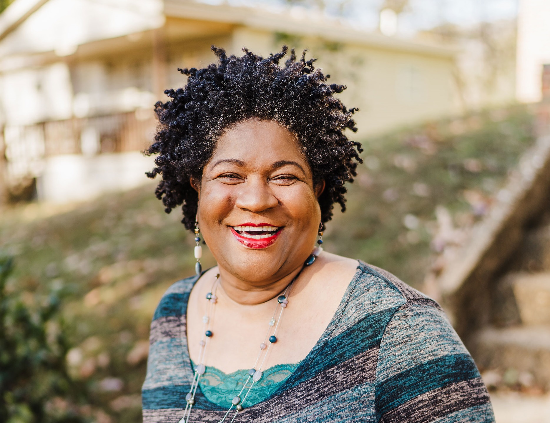An african american woman smiling in front of a house.