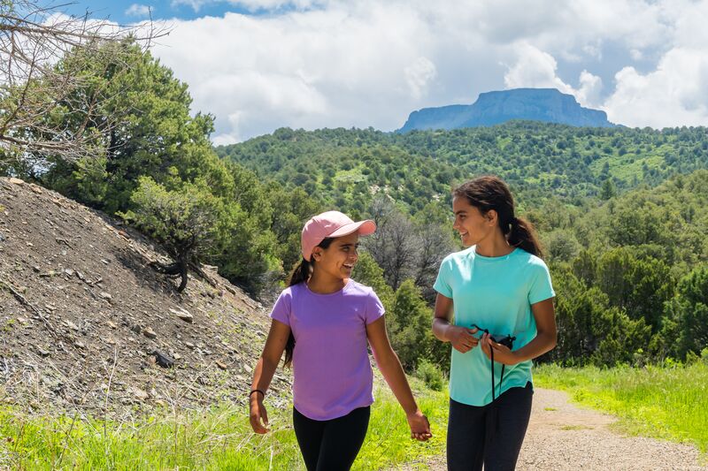 Two girls walking down a trail with mountains in the background.