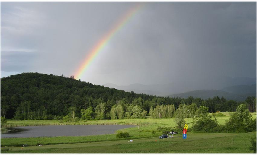 A rainbow over a green field with a mountain in the background