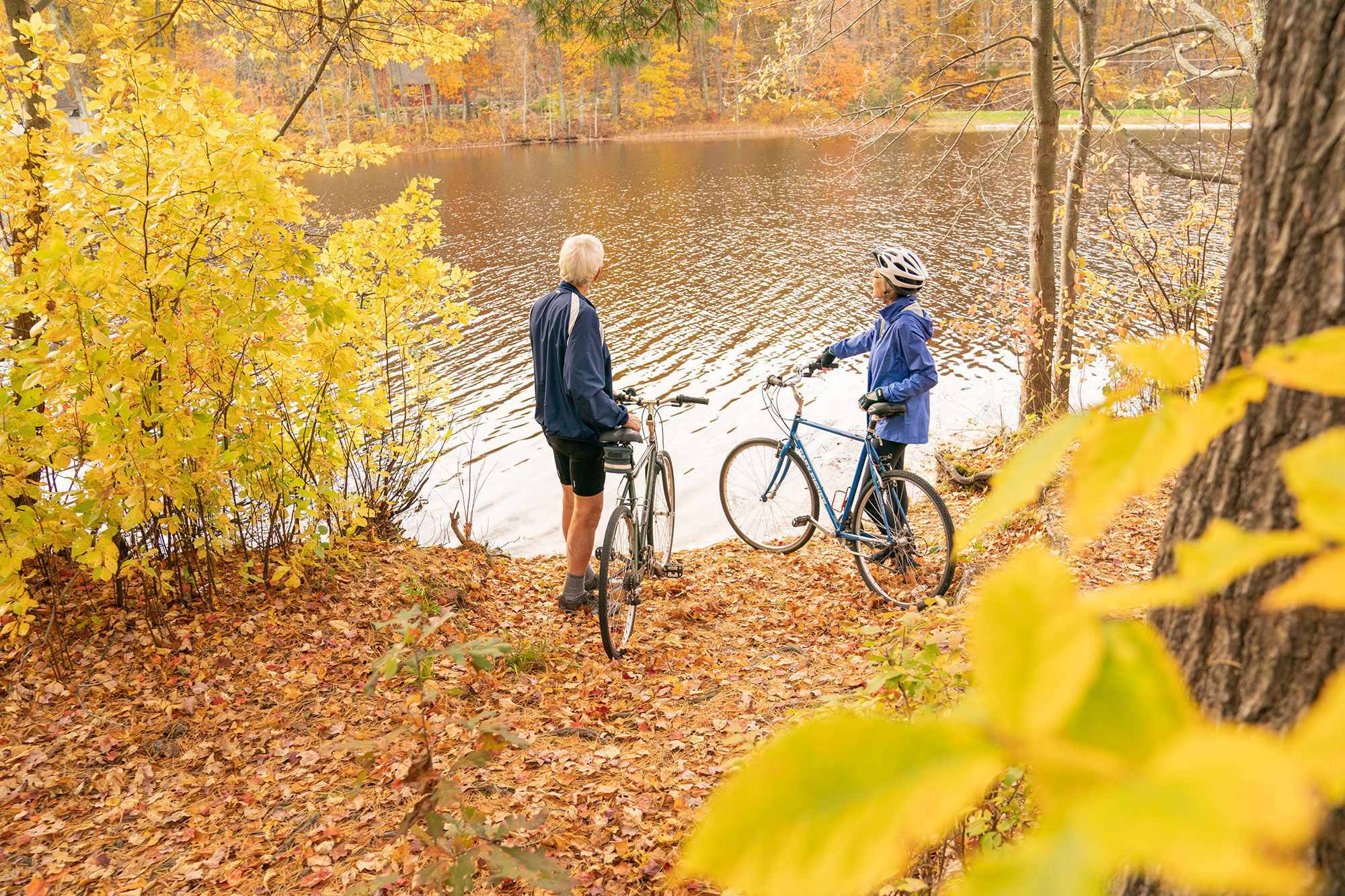 Two people standing near a lake with their bicycles.