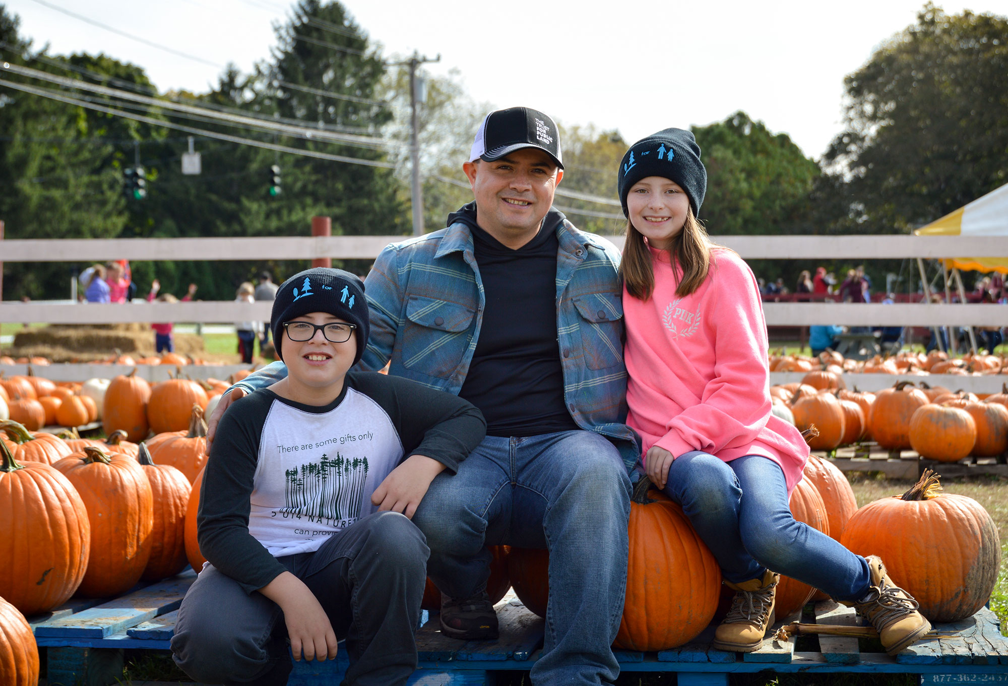 A man and two children posing for a photo in front of pumpkins.