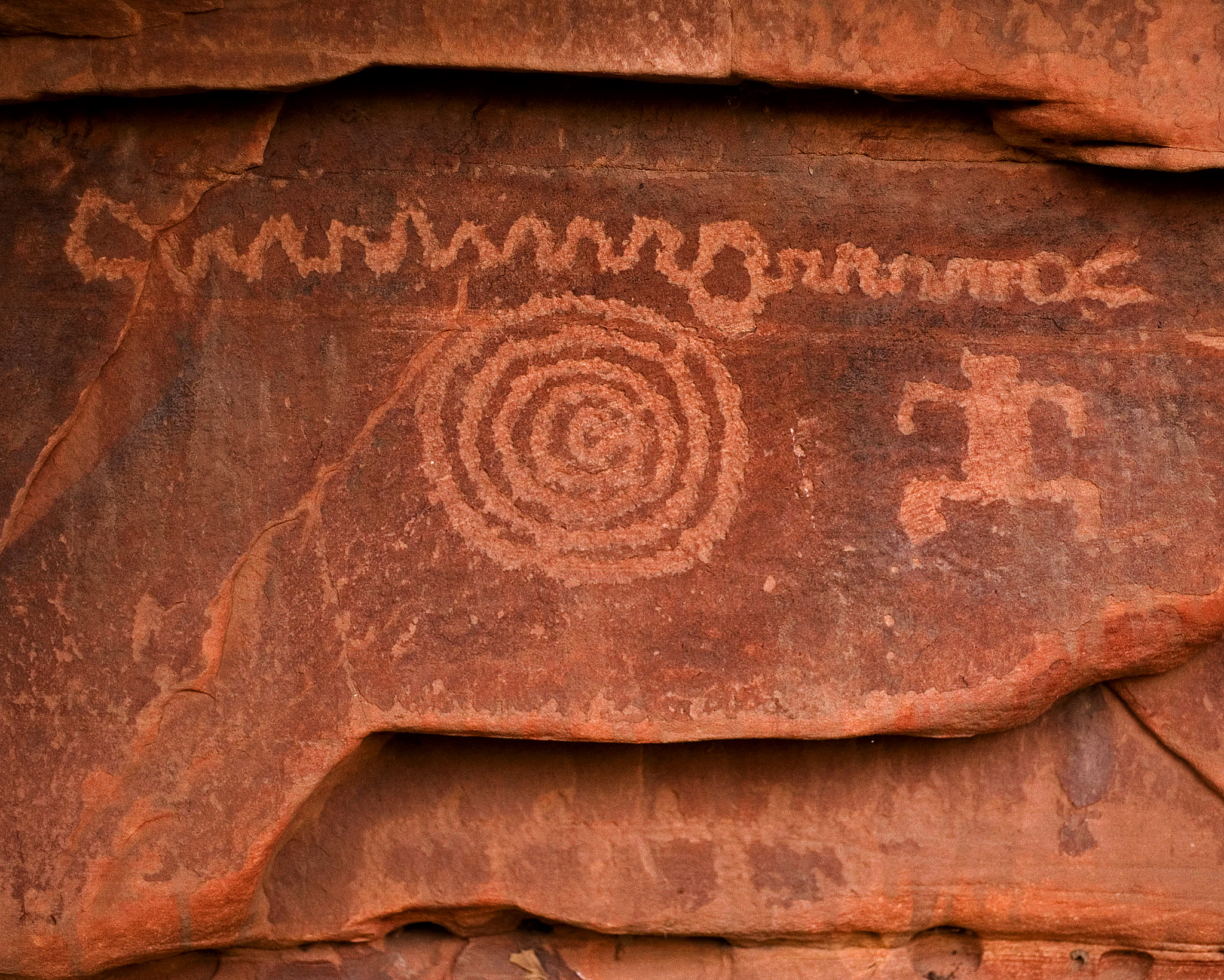 A rock art panel with a squiggly line, a human figure, and a spiral