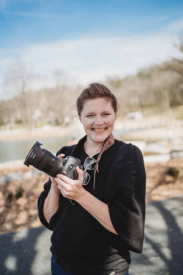A woman holding a camera in front of a lake.