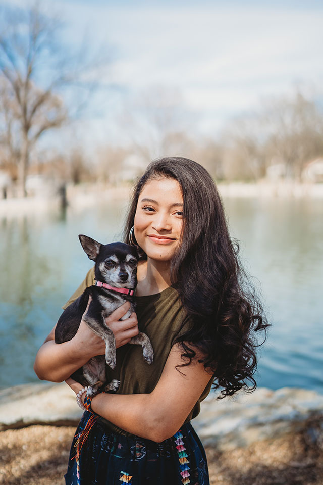 A young woman holding a chihuahua in front of a lake.