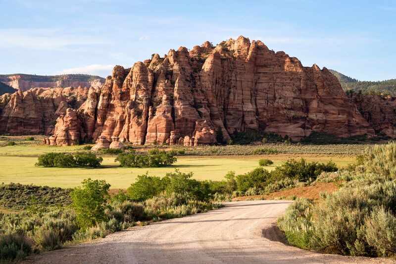 A dirt road leads to a red rock formation.