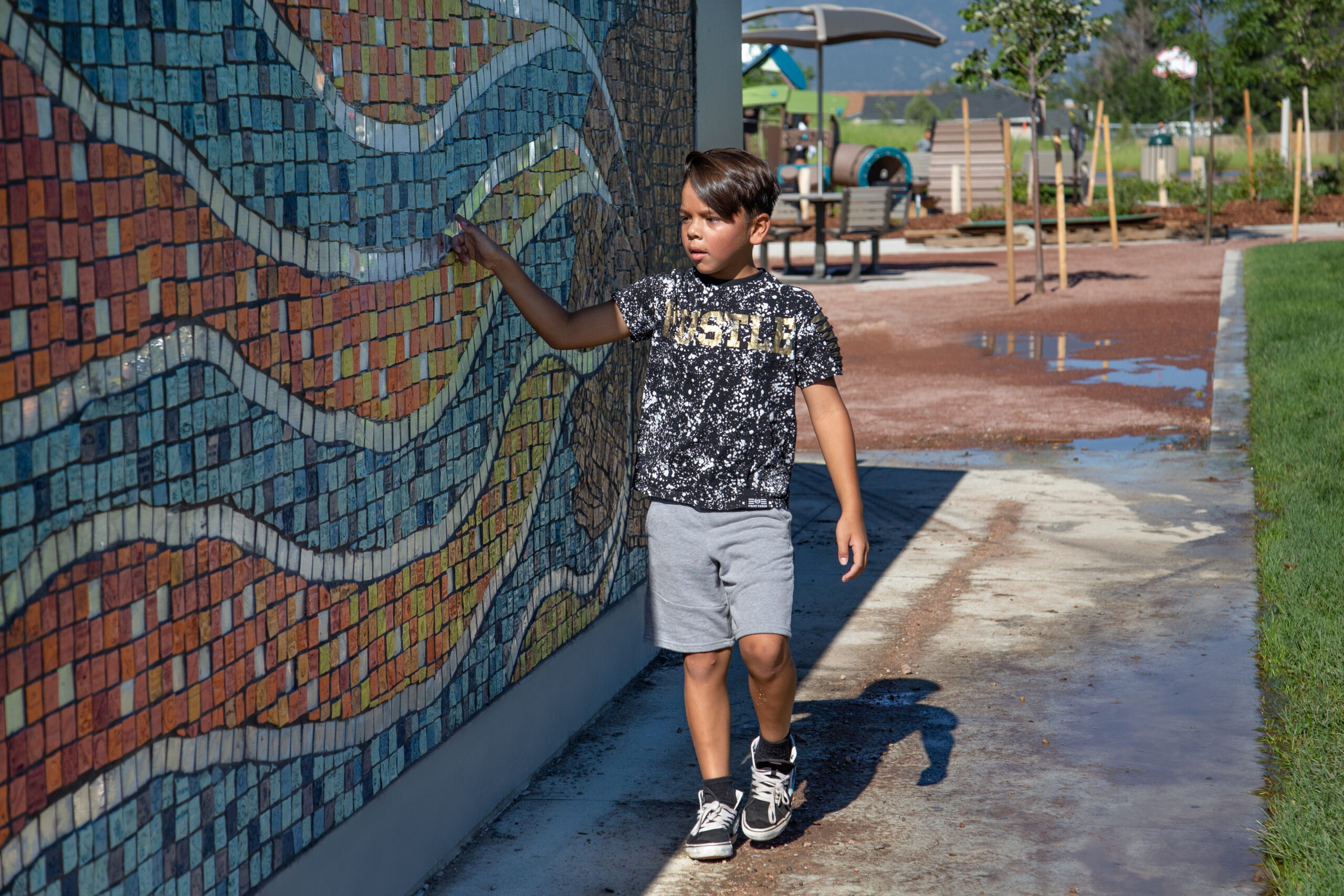 A boy explores a colorful mosaic reflecting community values, touching his hand to the wall as he walks by. 