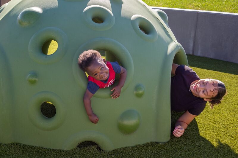 A woman and child play in a green play structure.