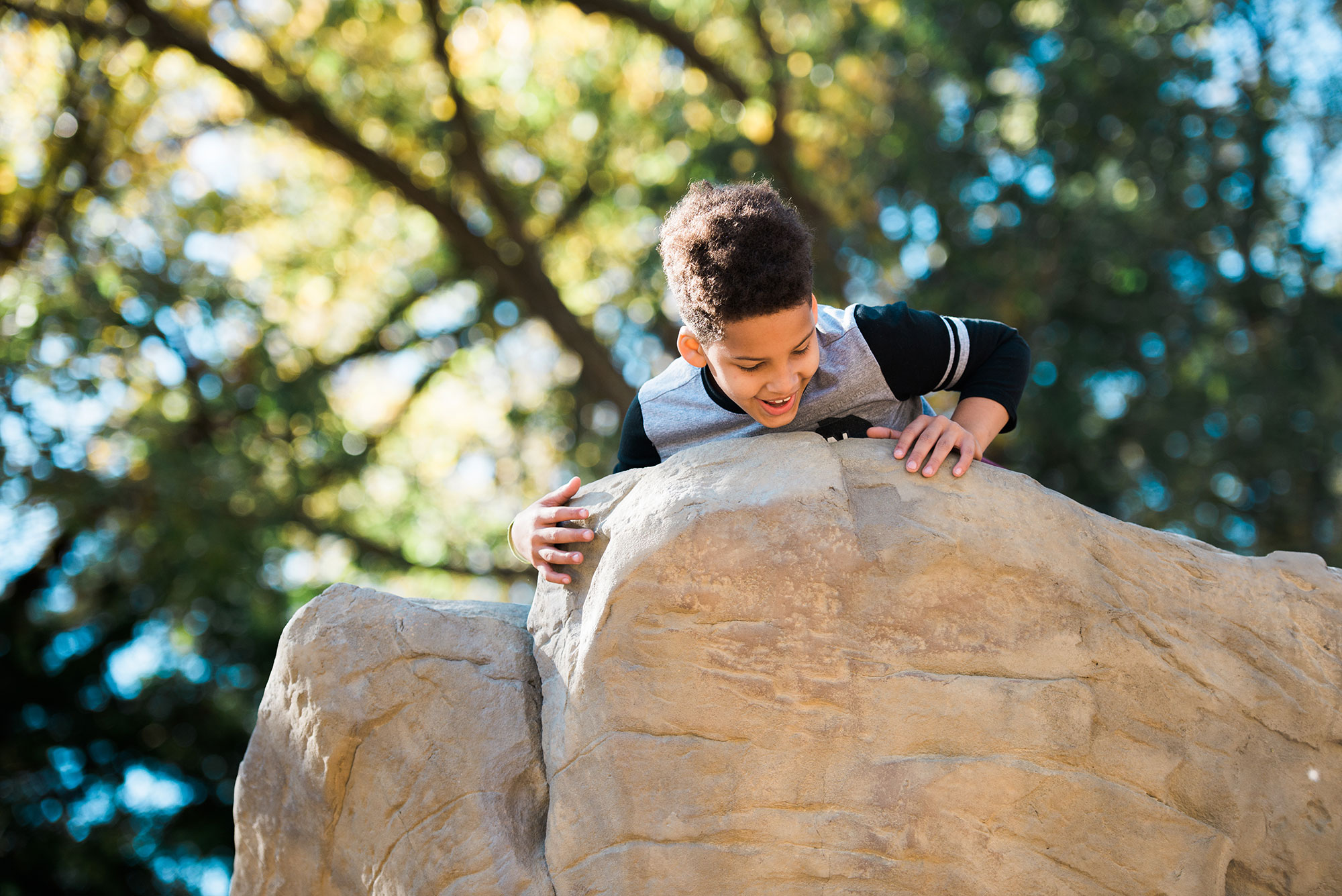 A boy climbing on a rock in a park.