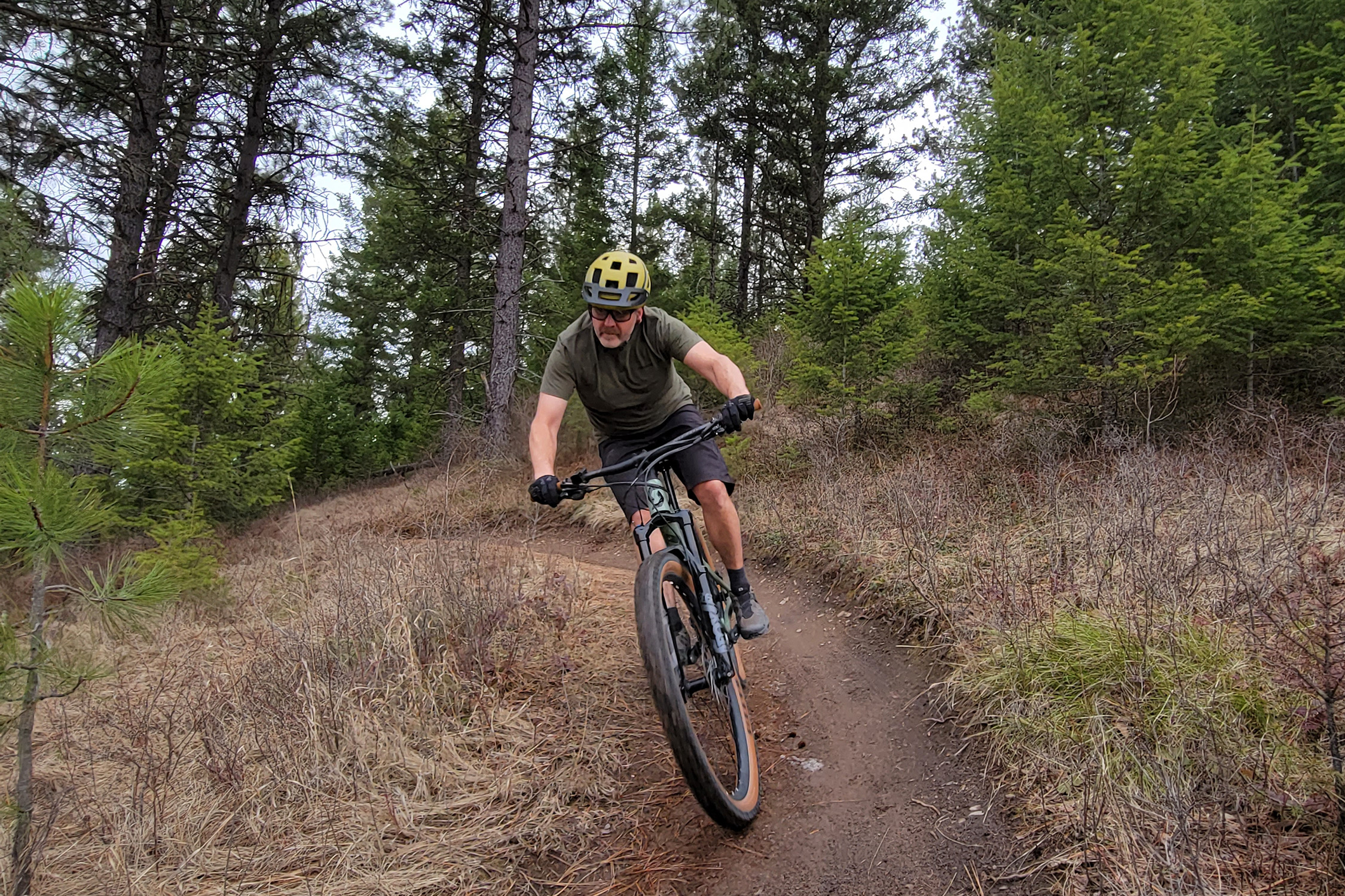 A white man in a helmet rides a mountain bike down a dirt trail.