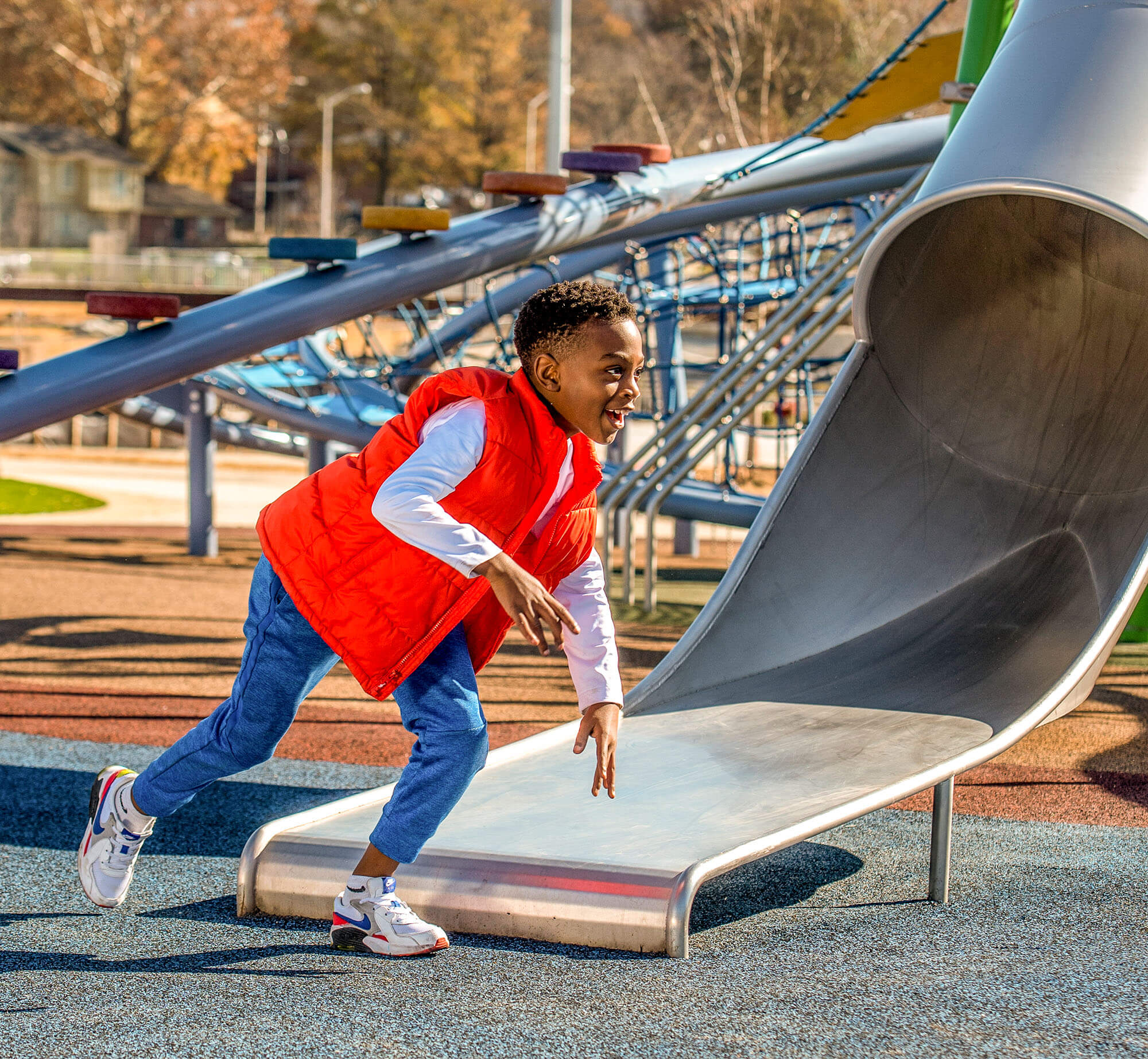 A boy is running down a slide at a playground.