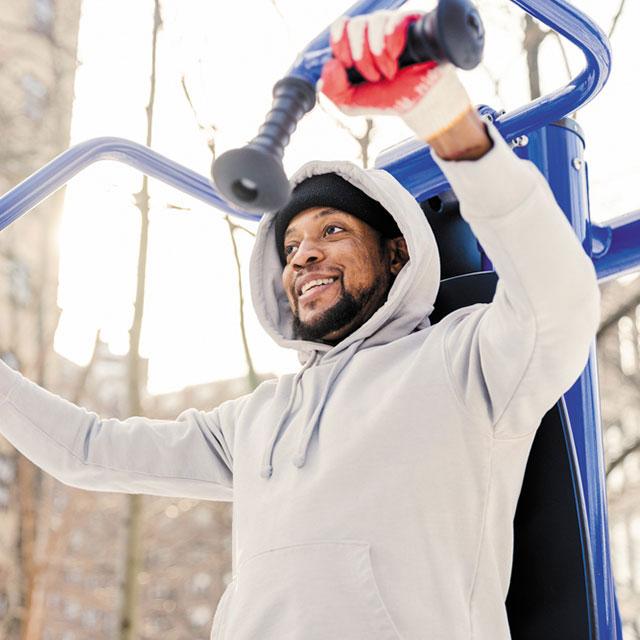 A man in a hoodie lifting weights in a park.