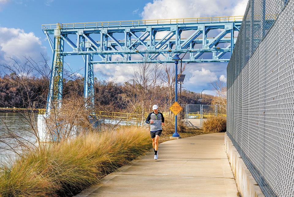 A runner is running along a path near a bridge.