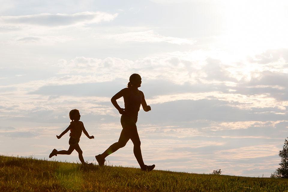 A silhouette of a mother and child jogging on a hill.