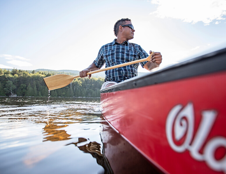 A man paddles a red canoe on a lake.