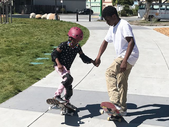 A boy helps a young girl learn how to skateboard