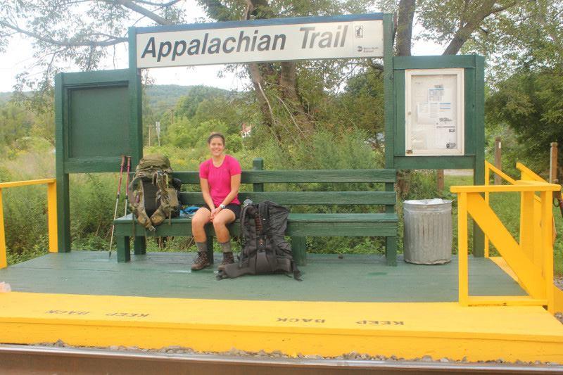 A woman with a backpack sits on the A.T. train stop bench